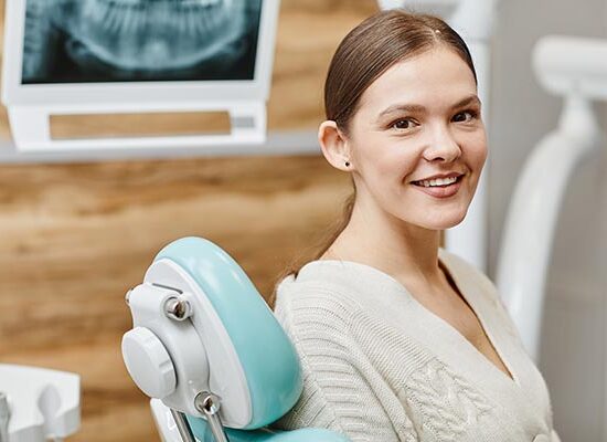 Portrait of young woman smiling at camera with while teeth while sitting in chair at dental clinic, copy space